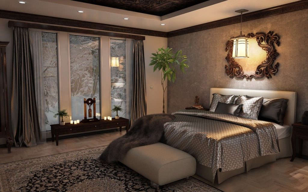Quarto de luxo em que há espelho na parede da cama e luminárias branco quente.