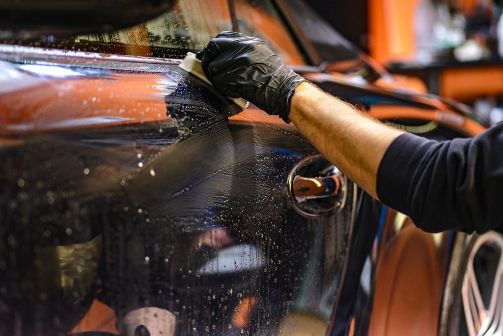 Na foto, há uma mão masculina limpando a lataria de um carro.
